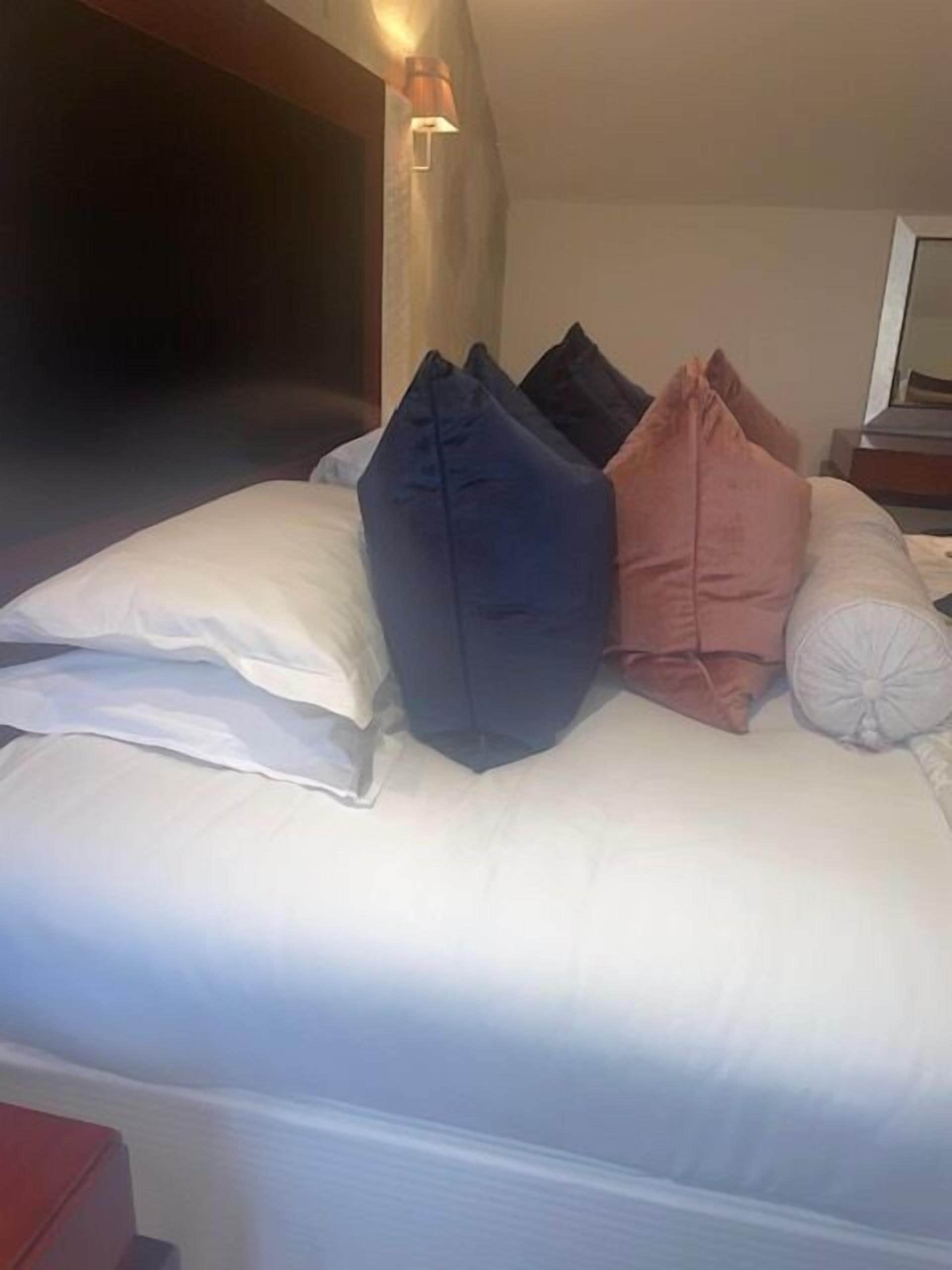 A neatly made bed with white and colored pillows, a headboard, and a bedside table with a lamp.