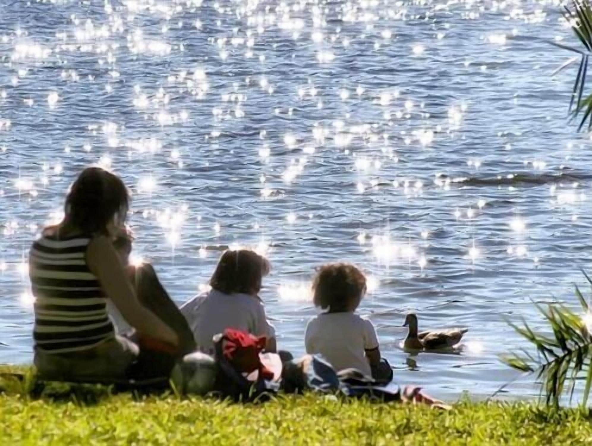 Una familia sentada junto a un lago con un pato.