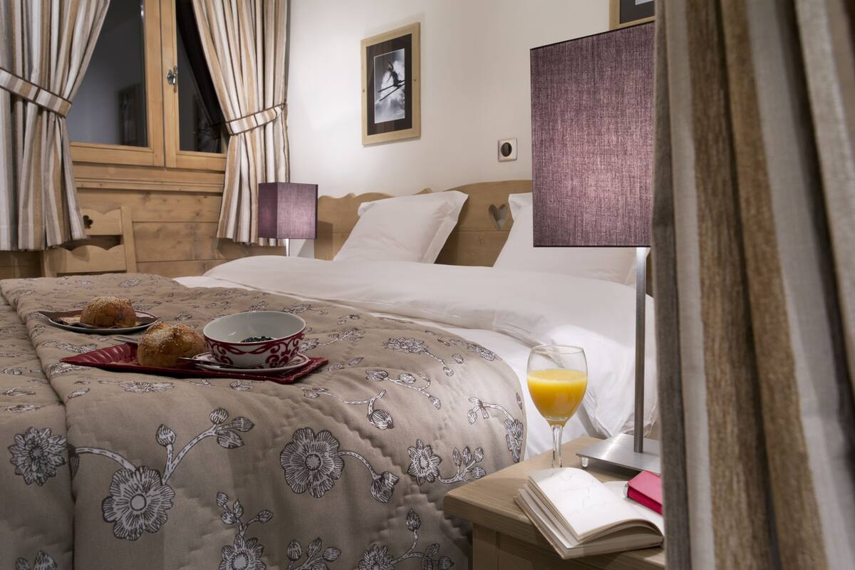 Een hotelkamer met een bed, een nachtkastje met een glas sinaasappelsap, een kom cornflakes en een dienblad met gebak.