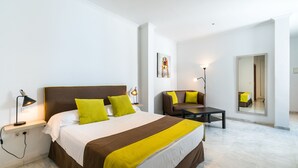 Una habitación de hotel moderna con una cama grande, un sofá, una mesita y un espejo.