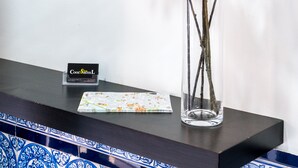 Un cuadro enmarcado en una pared, un florero transparente con ramas sobre una mesa, y una tarjeta de presentación.