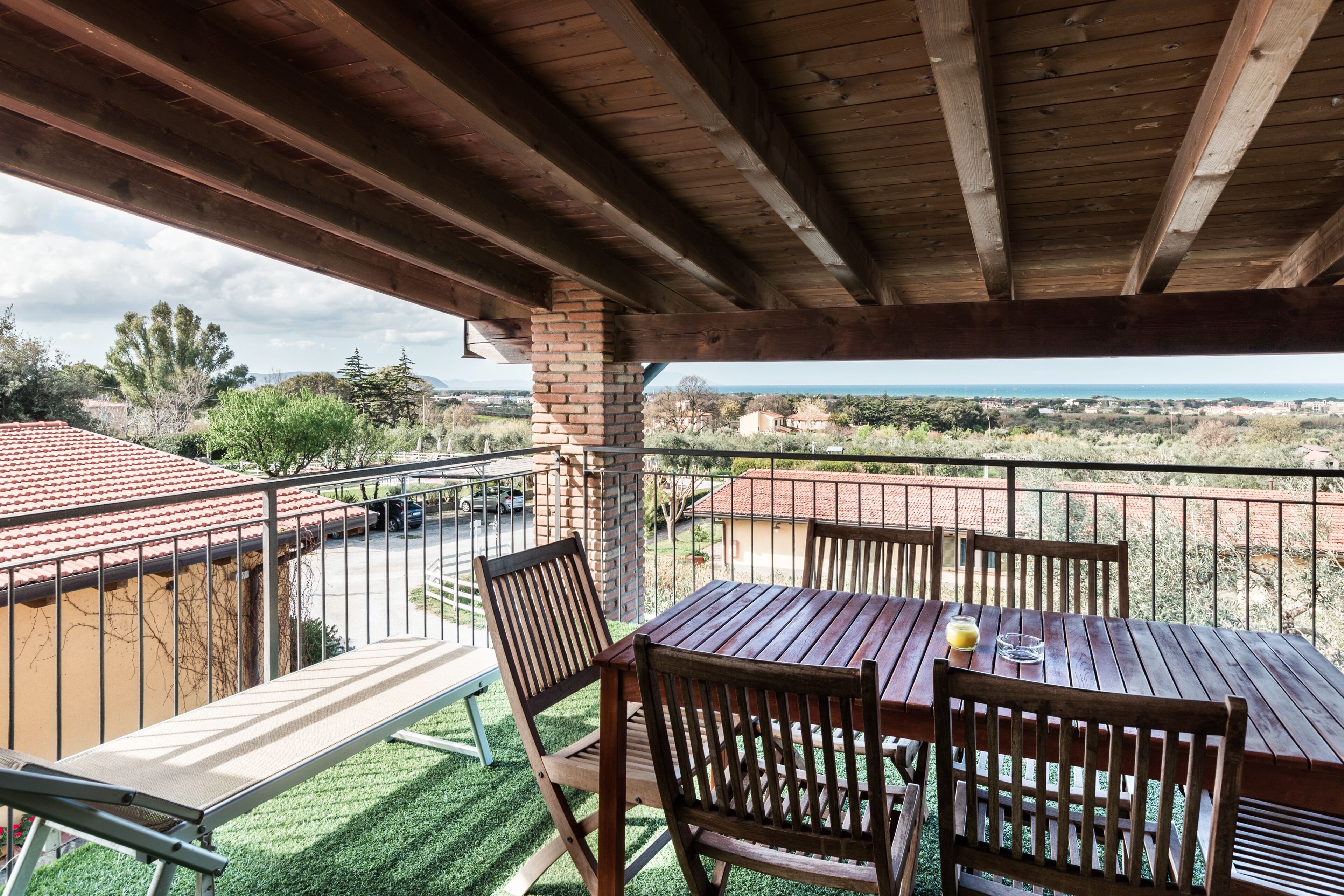 A wooden deck with a table and chairs, overlooking a scenic landscape with a view of the sea and distant buildings.