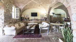 Una sala rústica con paredes y piso de piedra, un sofá, una mesa de centro, un televisor y un comedor con sillas y una mesa.