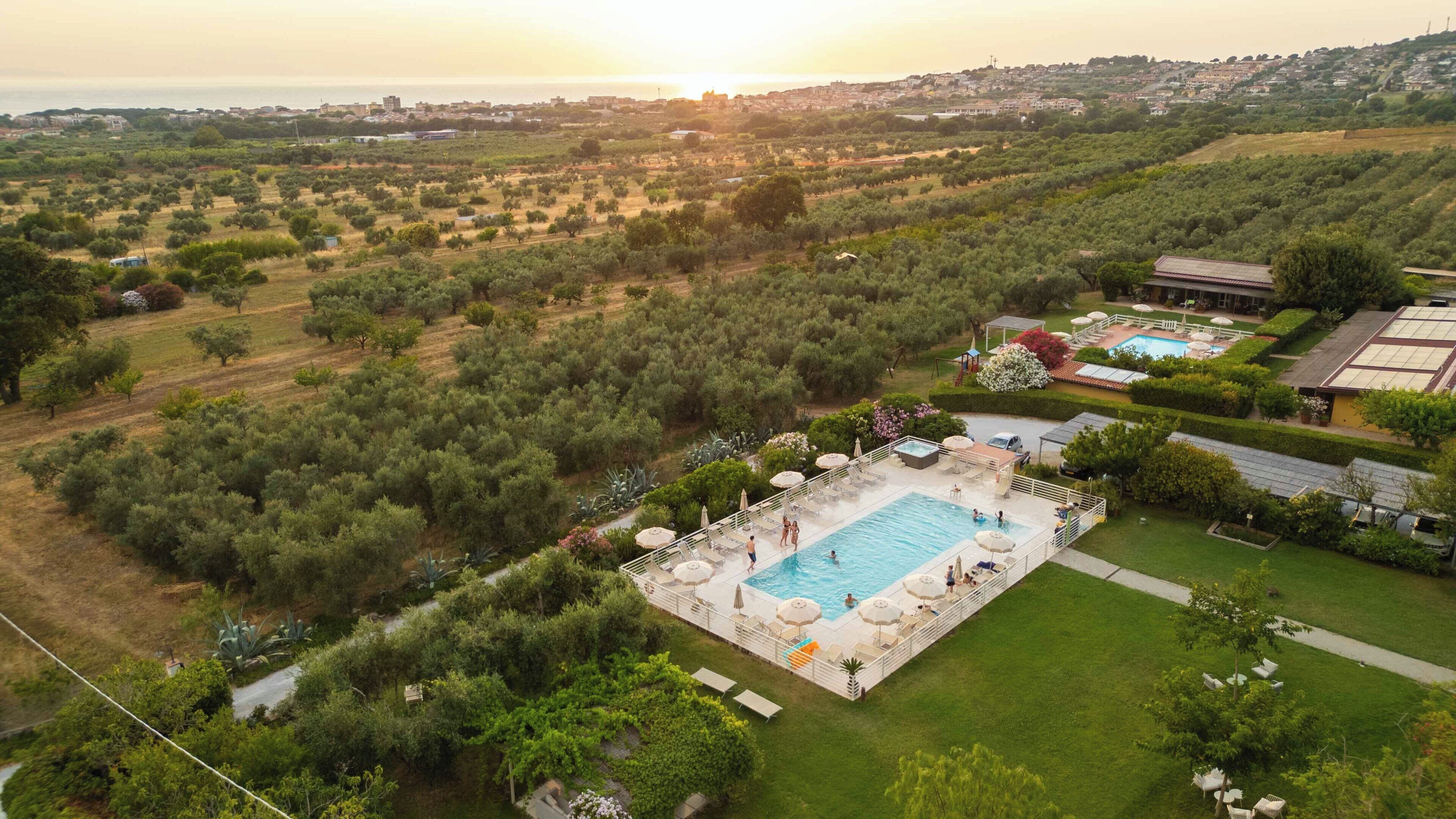 A pool area with lounge chairs and umbrellas, surrounded by greenery and a view of the sea.