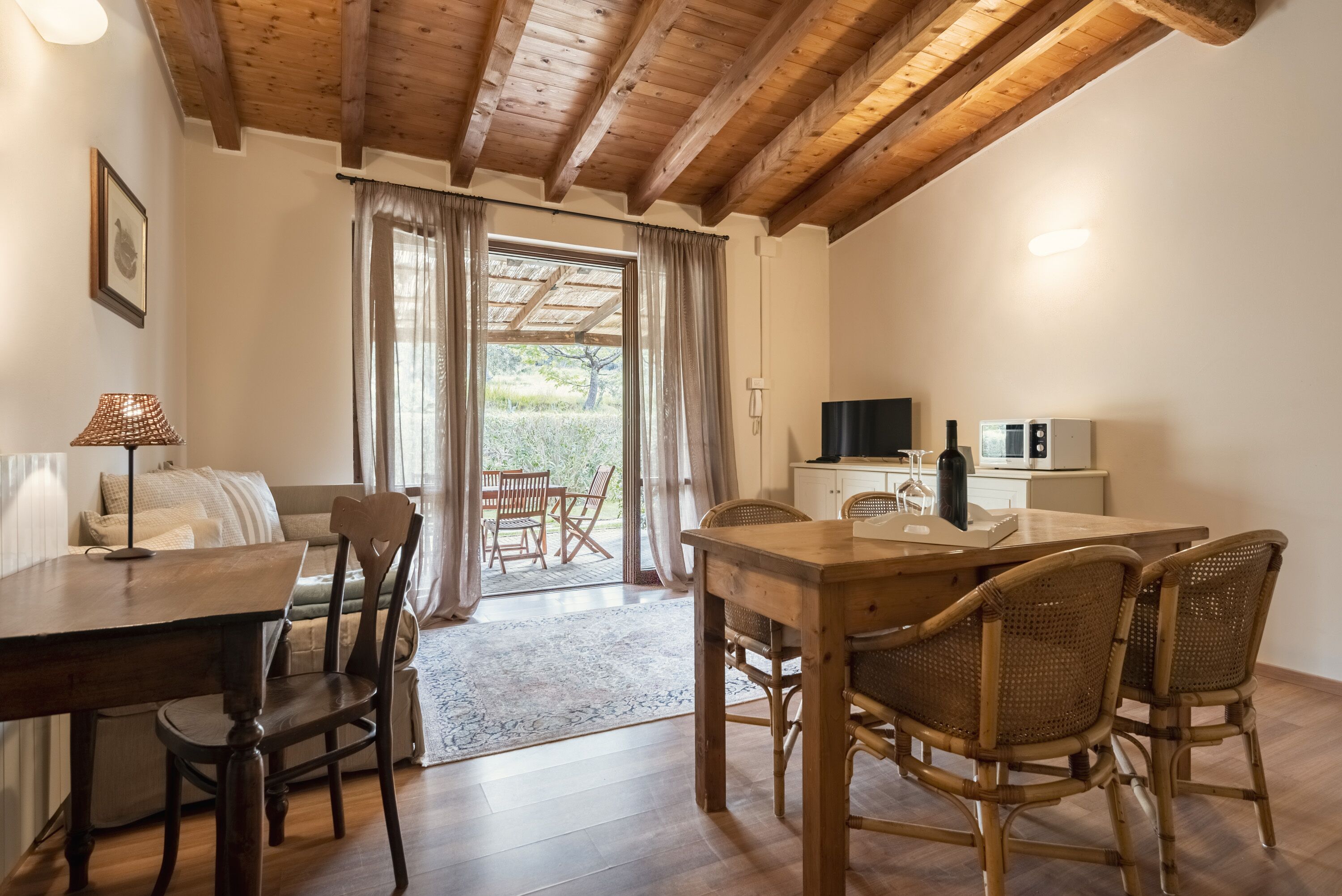 A cozy room with a wooden dining table, wicker chairs, a sofa, and a kitchen area with appliances.