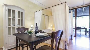Un comedor con una mesa preparada para dos, un aparador con puertas de vidrio y una cama con dosel y cortinas blancas.