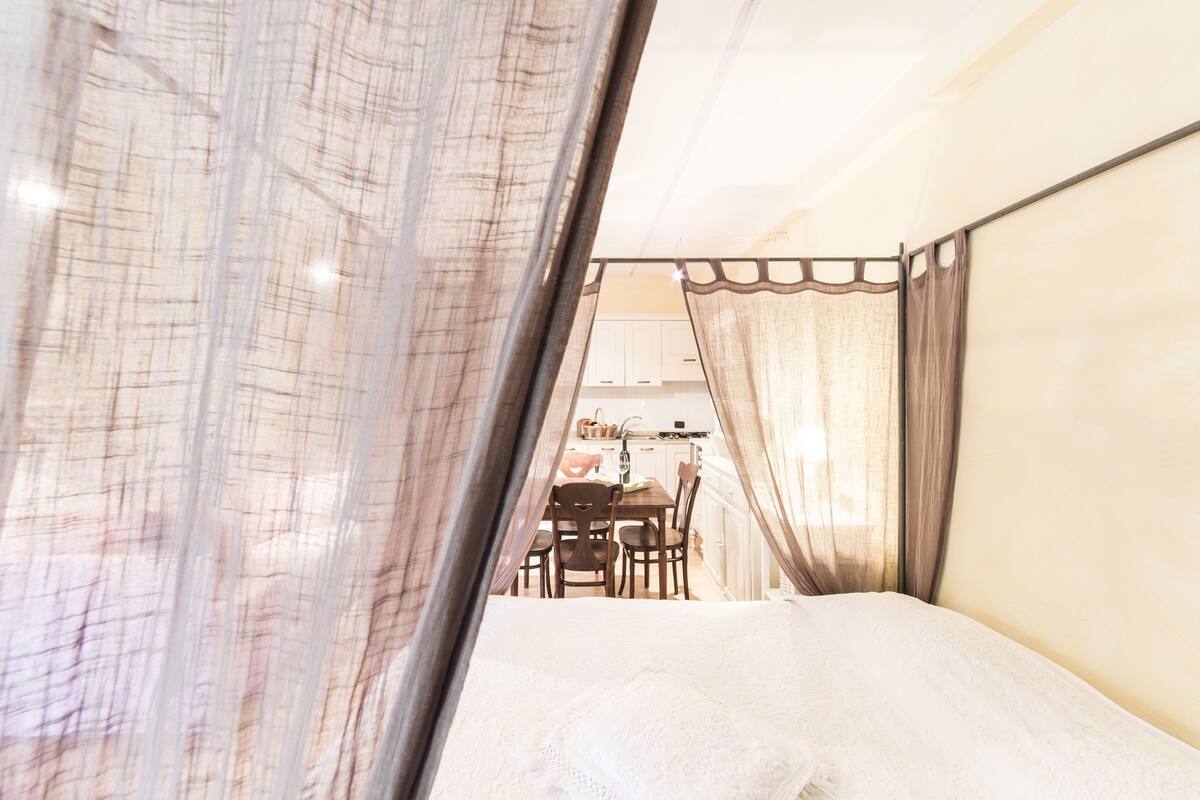 Um quarto com uma cama, uma mesinha e cadeiras ao fundo.