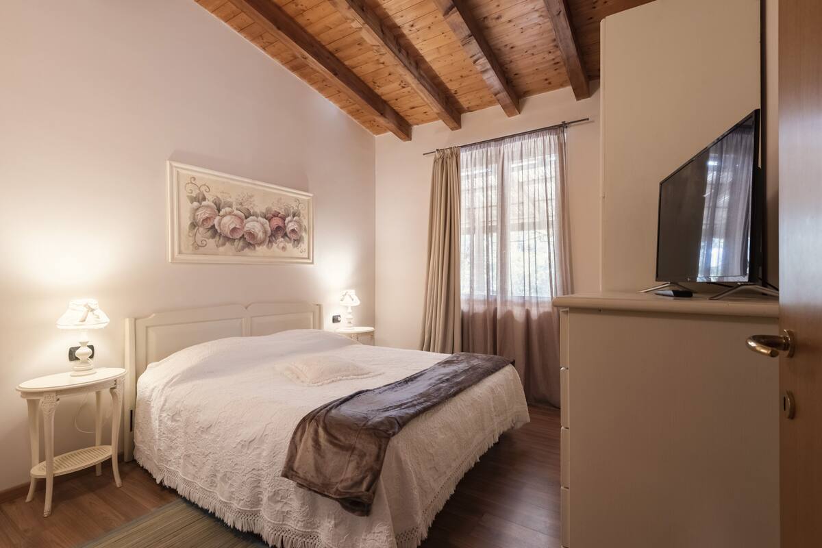 Um quarto com cama, mesas de cabeceira, televisão e guarda-roupa.