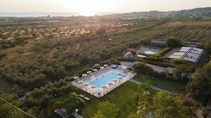 Vista aérea de una propiedad con piscina, abundante vegetación y una remota vista de un pueblo.