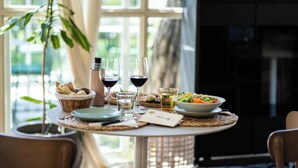 Una mesa de comedor con un cesto de pan, dos copas de vino tinto, un bol de ensalada y un plato de comida.