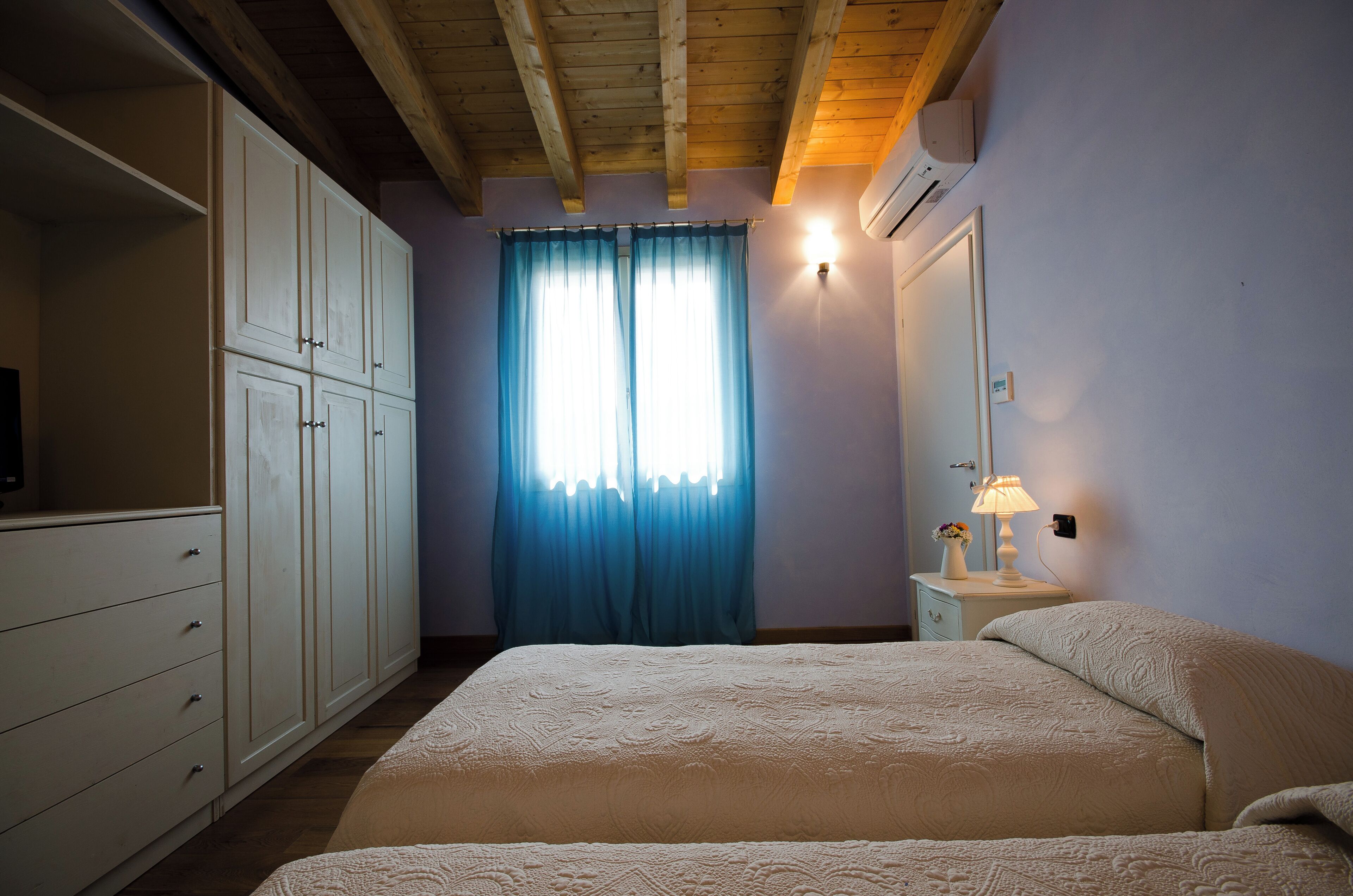 Une chambre à coucher avec un lit, une armoire, une table de chevet avec une lampe et une fenêtre avec des rideaux.