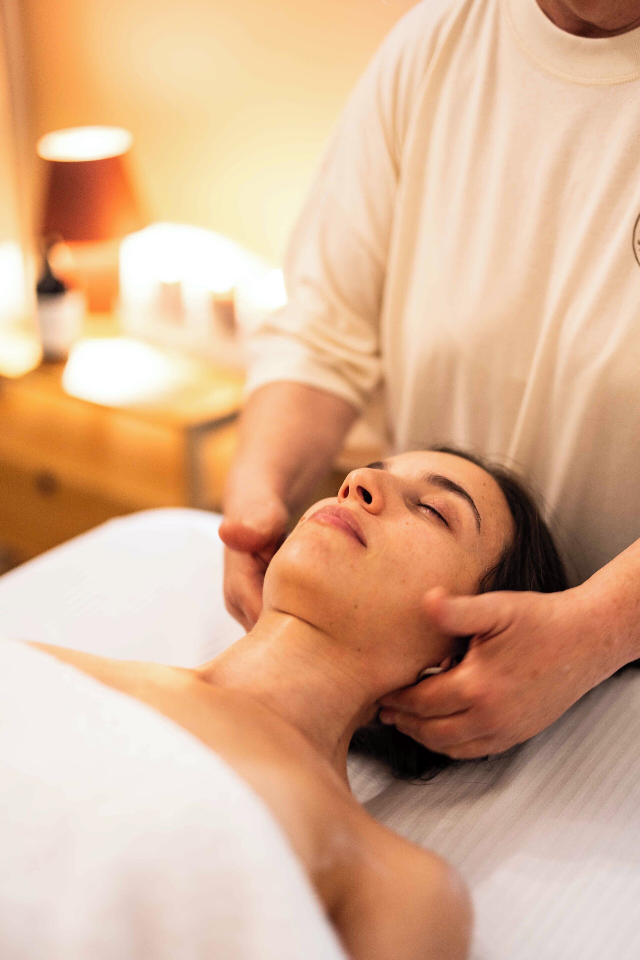 Iemand ontvangt een massage in een kamer met een bed, een nachtkastje en een lamp.