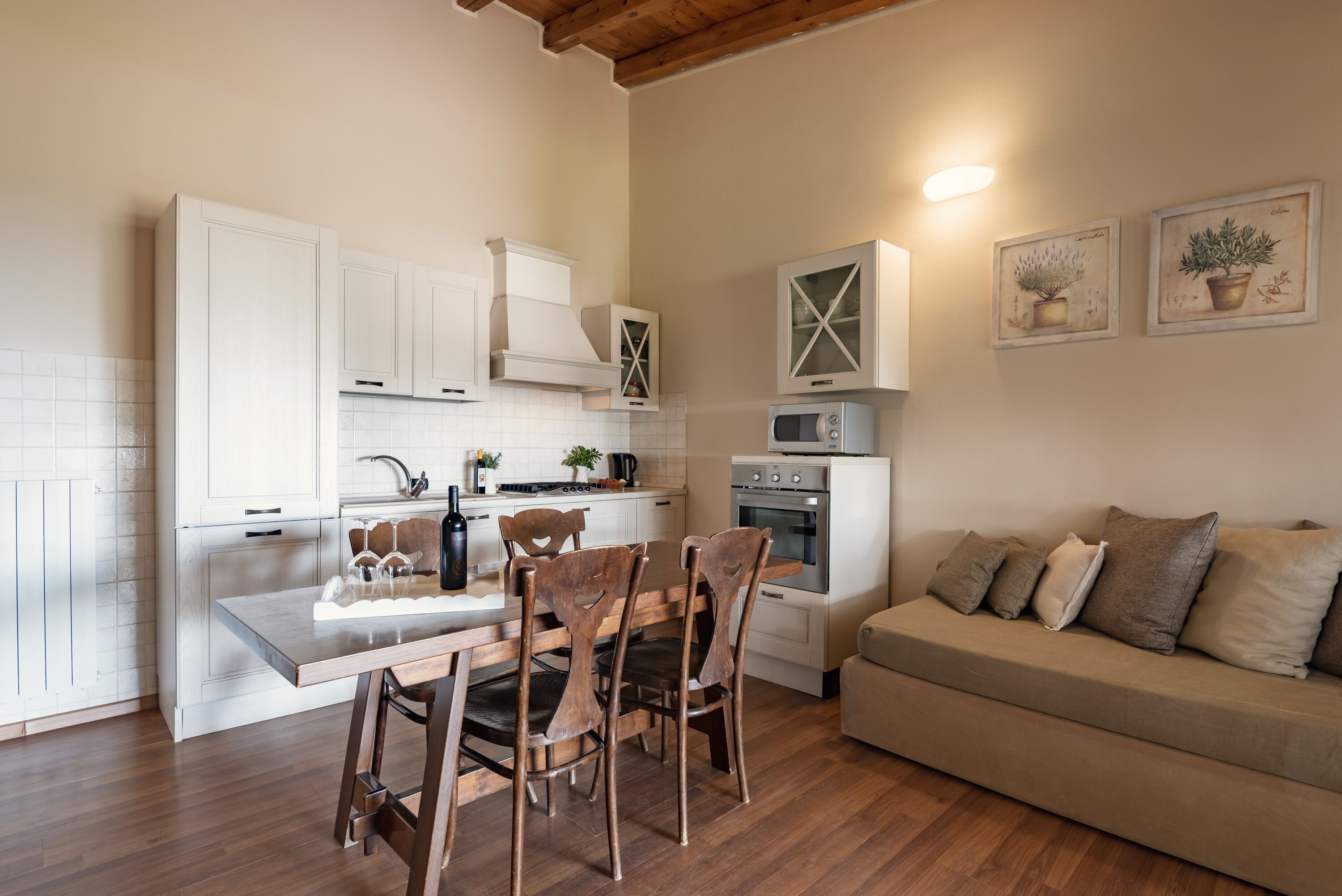 Une cuisine de taille réduite avec des meubles blancs, une table à manger en bois et un canapé beige.
