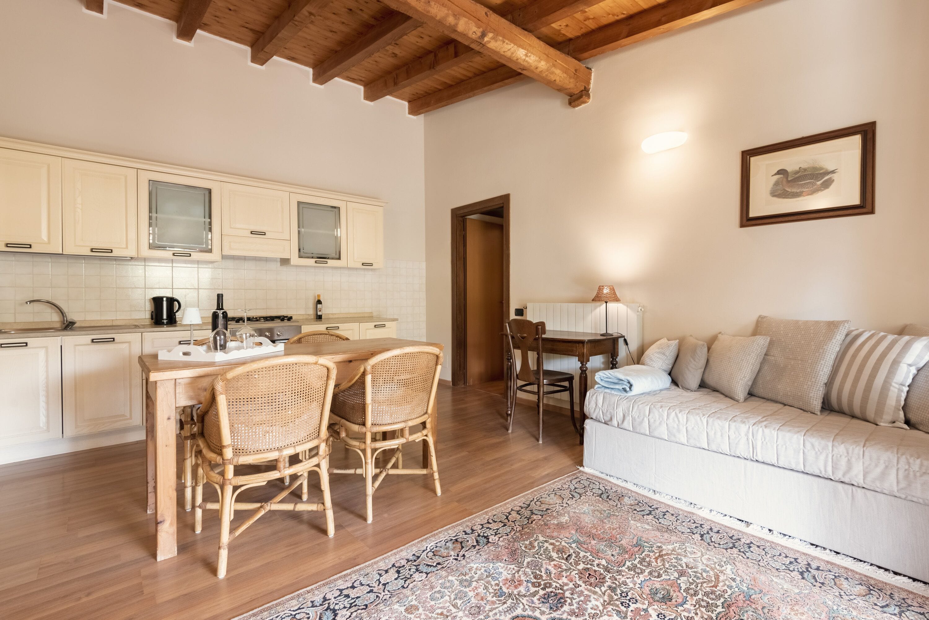 A kitchen with wooden cabinets, a dining table with chairs, a sofa, and a patterned rug.