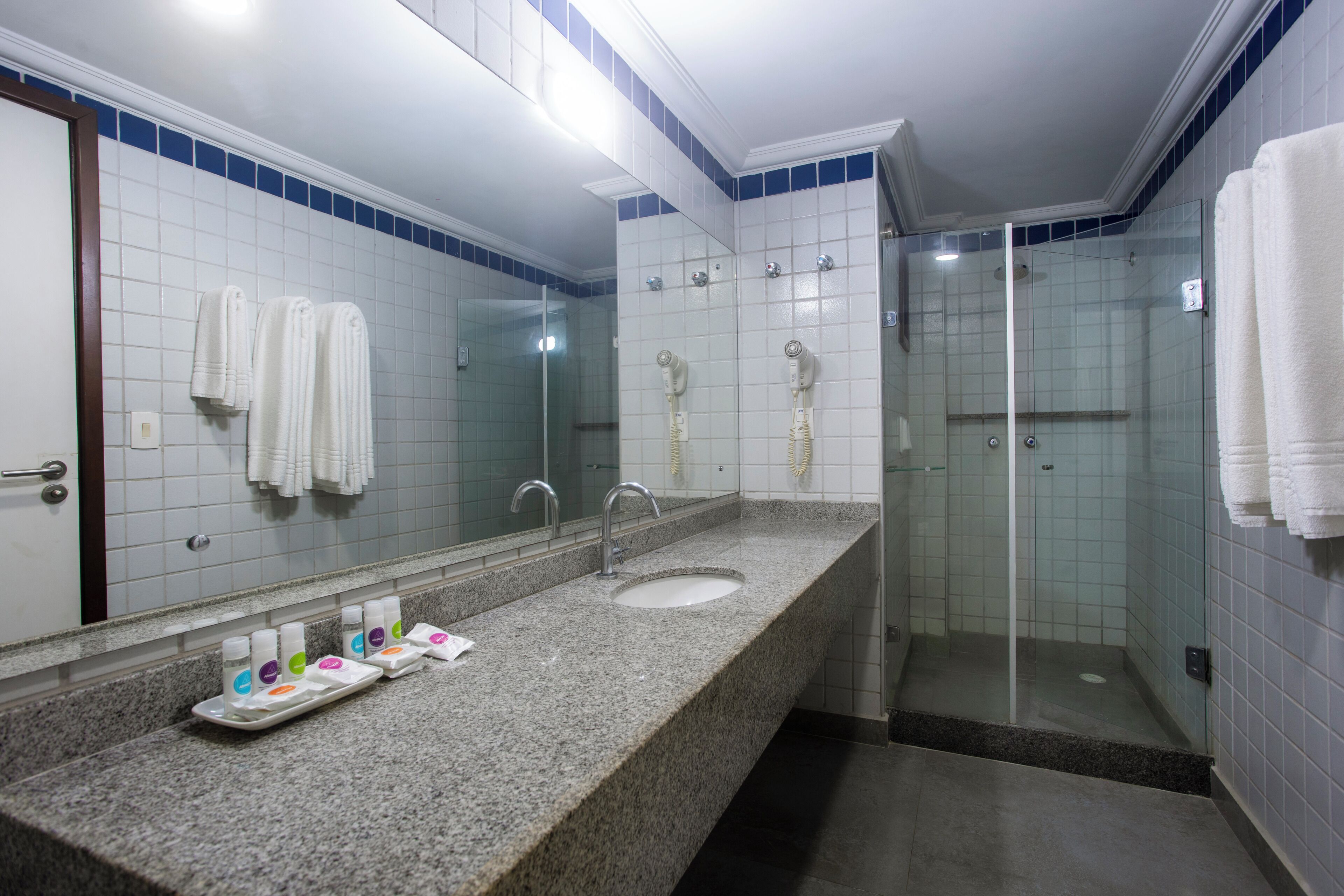 Un baño con encimera de granito, lavamanos, espejo y ducha con mampara de vidrio.