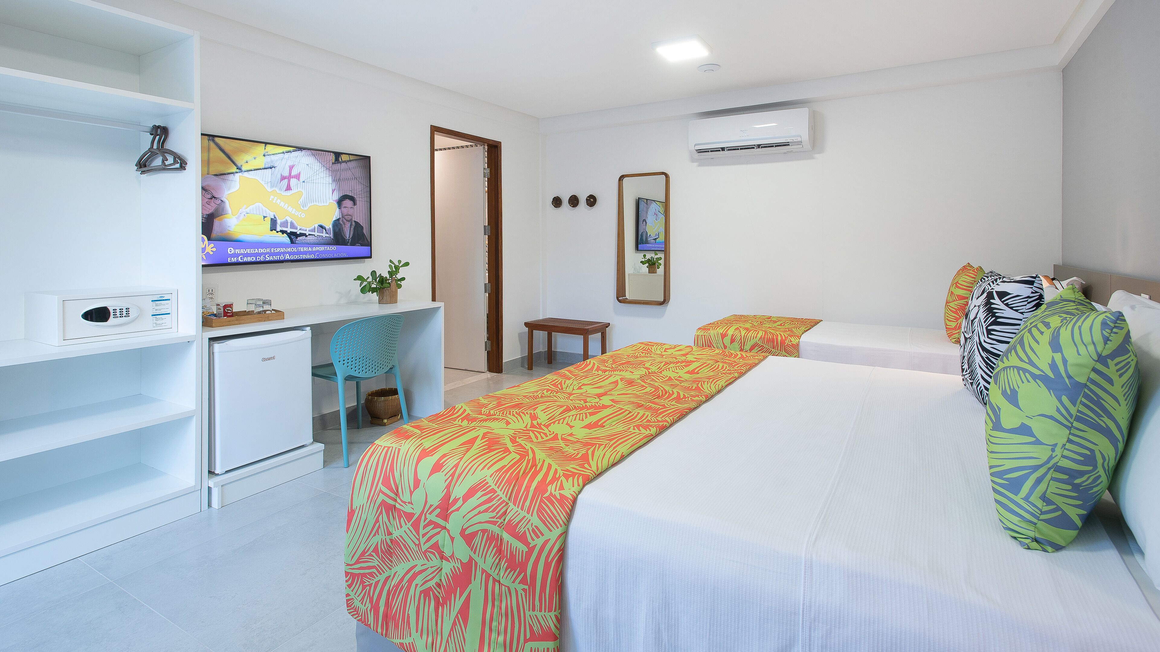 Quarto de hotel com cama, escrivaninha, televisão e ar condicionado.