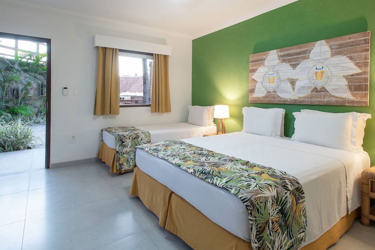 Ein Hotelzimmer mit einem großen Bett, zwei Einzelbetten, einer grünen Akzentwand und einem Fenster mit Vorhängen.