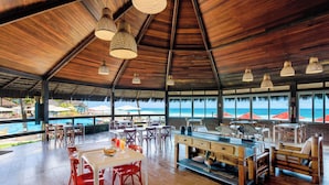 A spacious dining area with wooden flooring, tables, and chairs, overlooking a pool and beach. - Armação Resort Porto de Galinhas (Ipojuca)