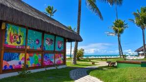 A colorful building with a thatched roof, surrounded by palm trees and a clear blue sky. - Armação Resort Porto de Galinhas (Ipojuca)