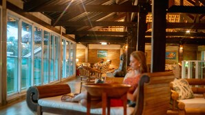 A cozy indoor seating area with wooden furniture and large windows. - Armação Resort Porto de Galinhas (Ipojuca)