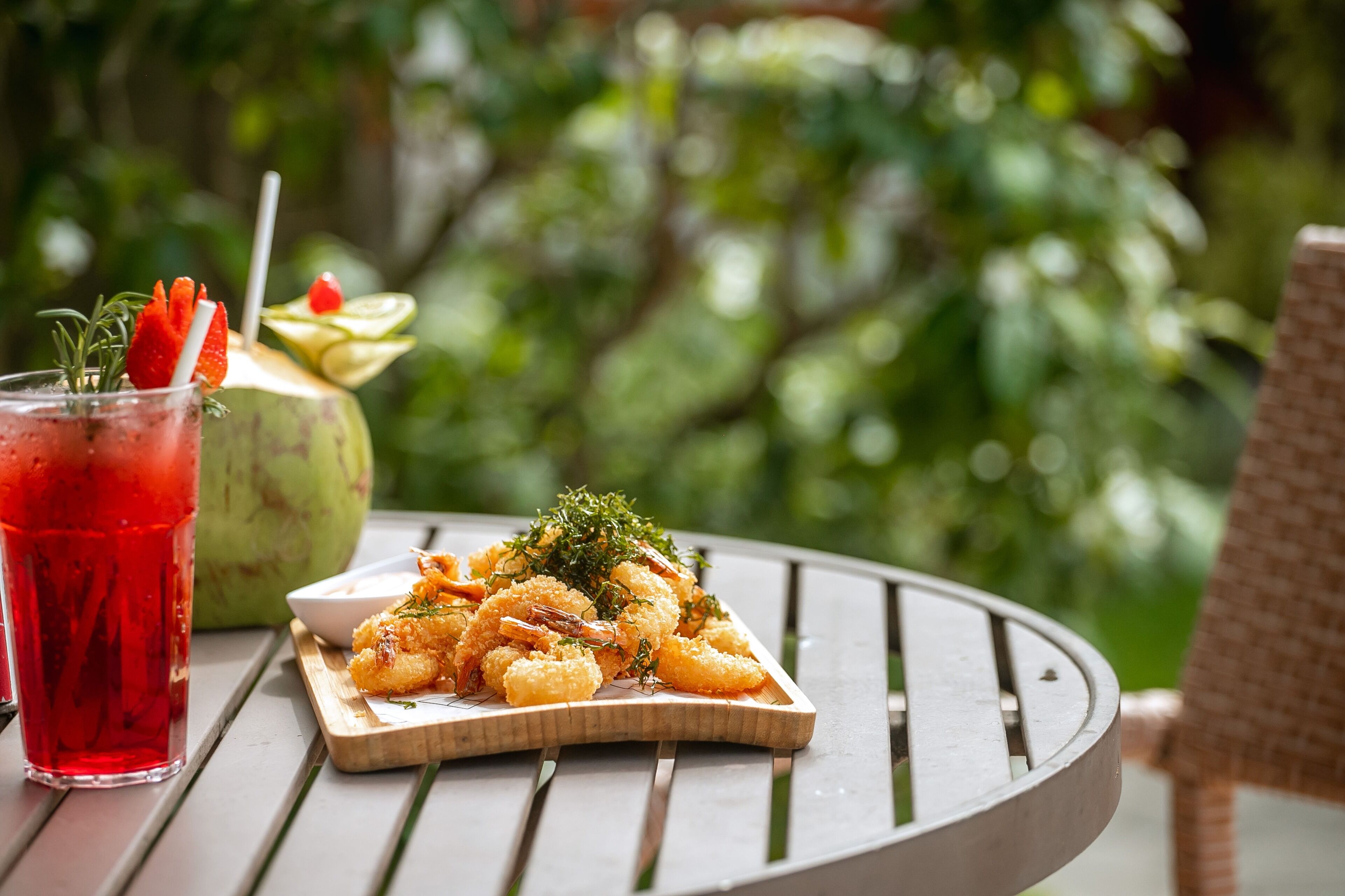 A meal of shrimp and a drink on a table with a natural backdrop.