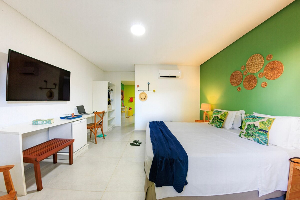 A hotel room with a bed, a desk with a laptop, a chair, a TV, and a wall with decorative plates.