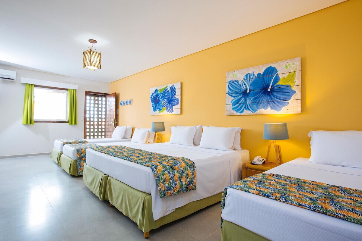 A hotel room with two beds, a window with curtains, a wall with floral artwork, and a lamp on a bedside table.