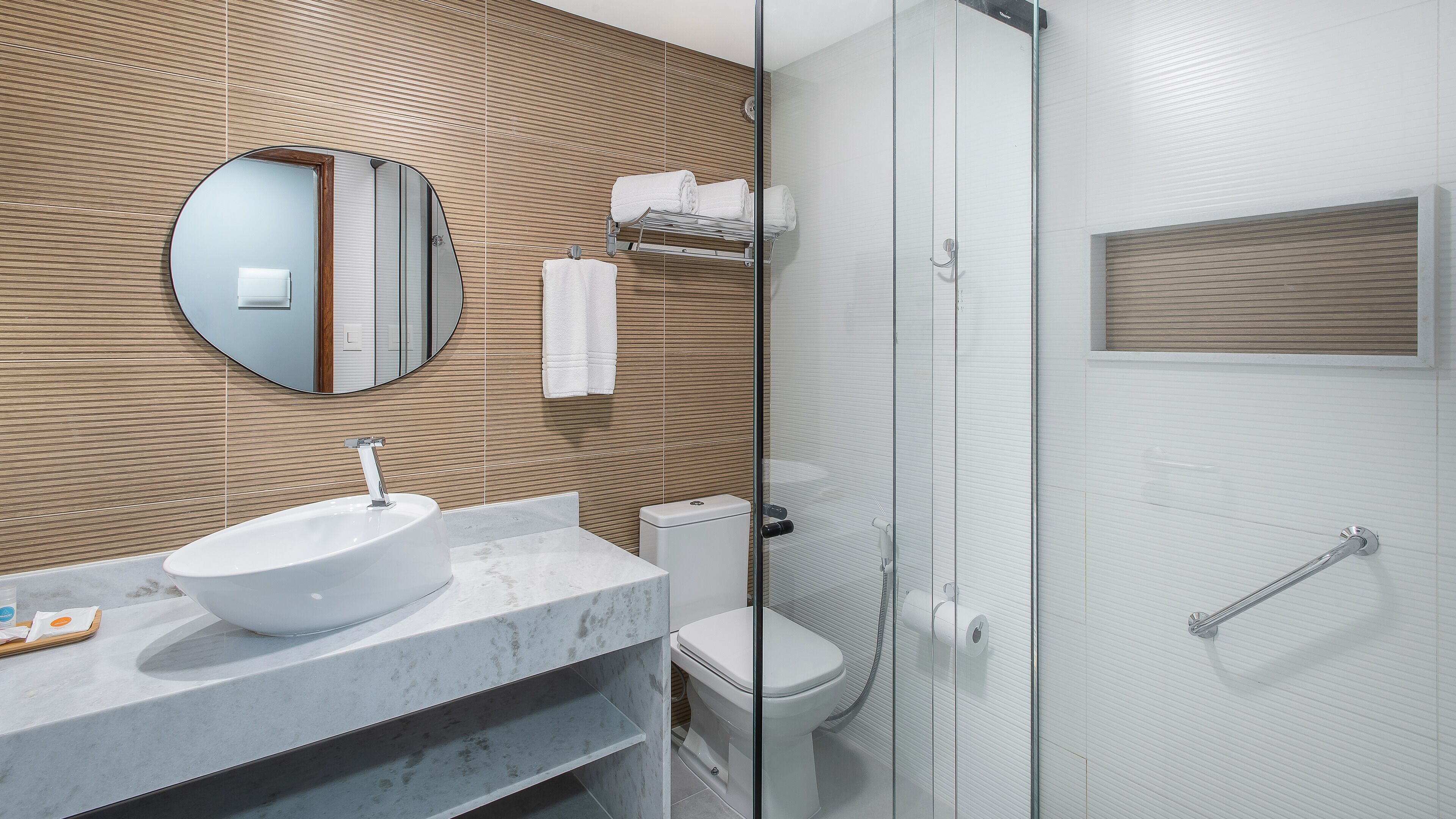 Een moderne badkamer met een ronde spiegel, een wit wastafelmeubel, een toilet en een douchecabine met glazen wanden.