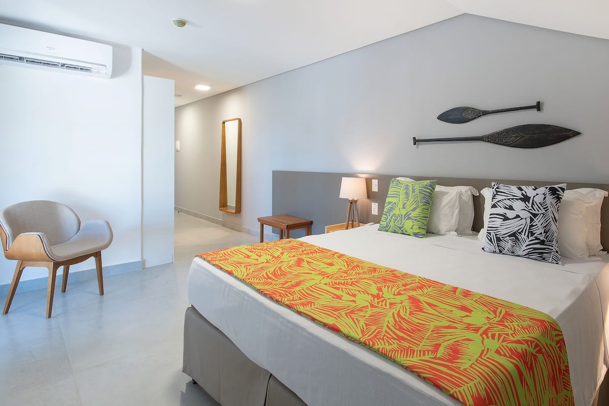 Ein modernes Hotelzimmer mit Bett, Sessel, Schreibtisch und Wandklimaanlage.