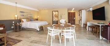 Una habitación de hotel moderna con una cama, una mesa de comedor con sillas, un televisor y un minibar.