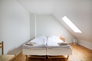 A small, single-room apartment with a sloped ceiling, two single beds, a wooden floor, a chair, a bedside table with a lamp, and a wall-mounted fan. - Motel Stege (Stege)