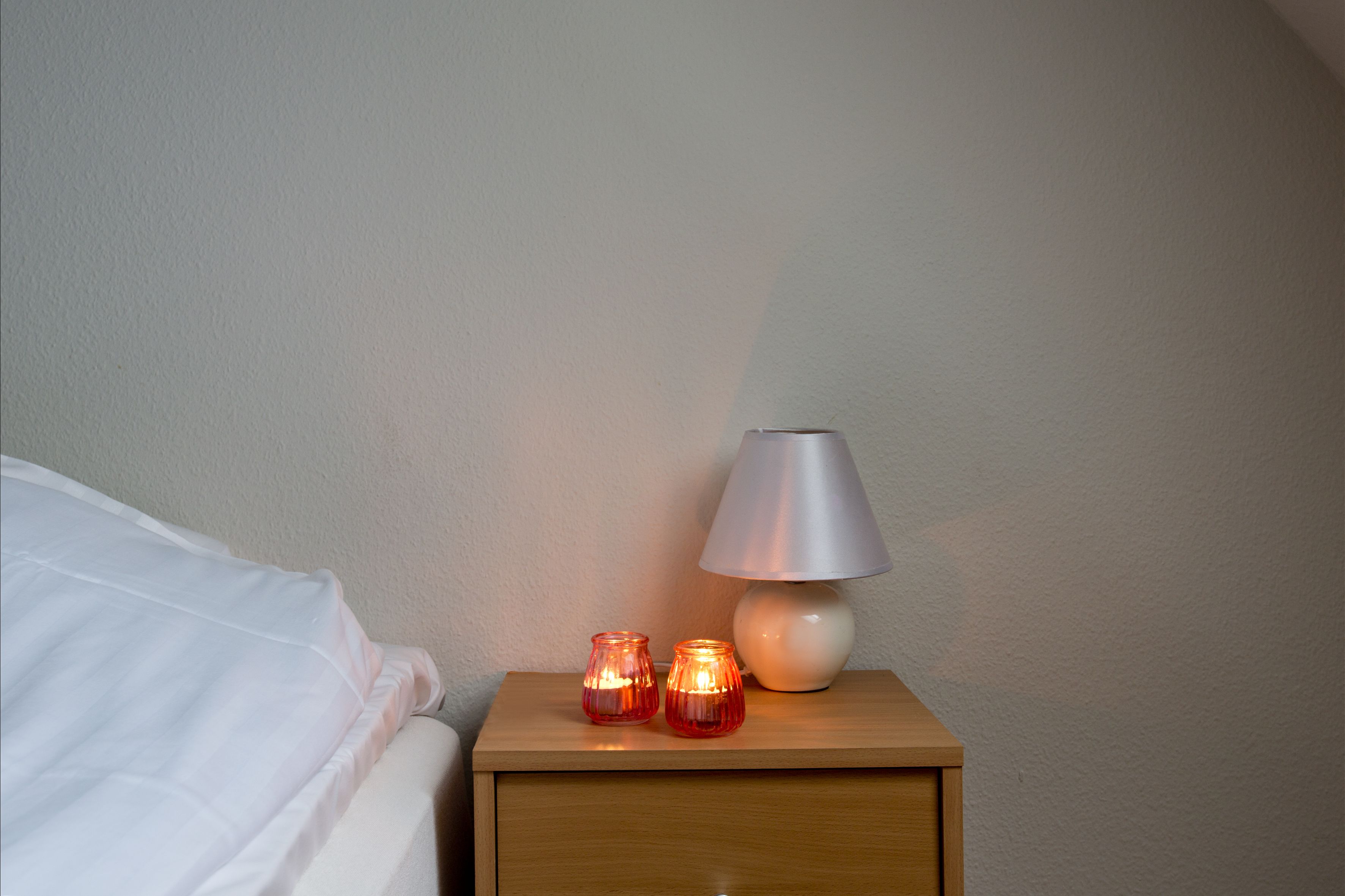 Et natbord i træ med en hvid lampe og to tændte stearinlys.