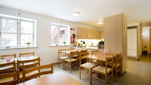 A dining area with wooden tables and chairs, a kitchen area with cabinets and appliances, and large windows providing natural light. - Motel Stege (Stege)