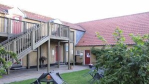 A building with a red-tiled roof, a staircase leading to a balcony, and outdoor seating with tables and chairs. - Motel Stege (Stege)