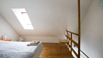 Une chambre avec un plafond en pente, un lit, une chaise, un ventilateur et une fenêtre.