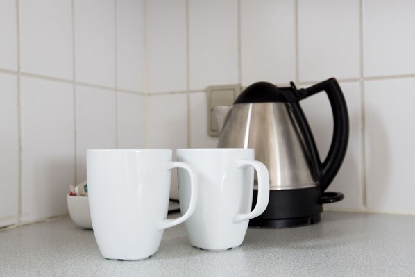 Two white mugs on a countertop with a black electric kettle in the background. - Motel Stege (Stege)