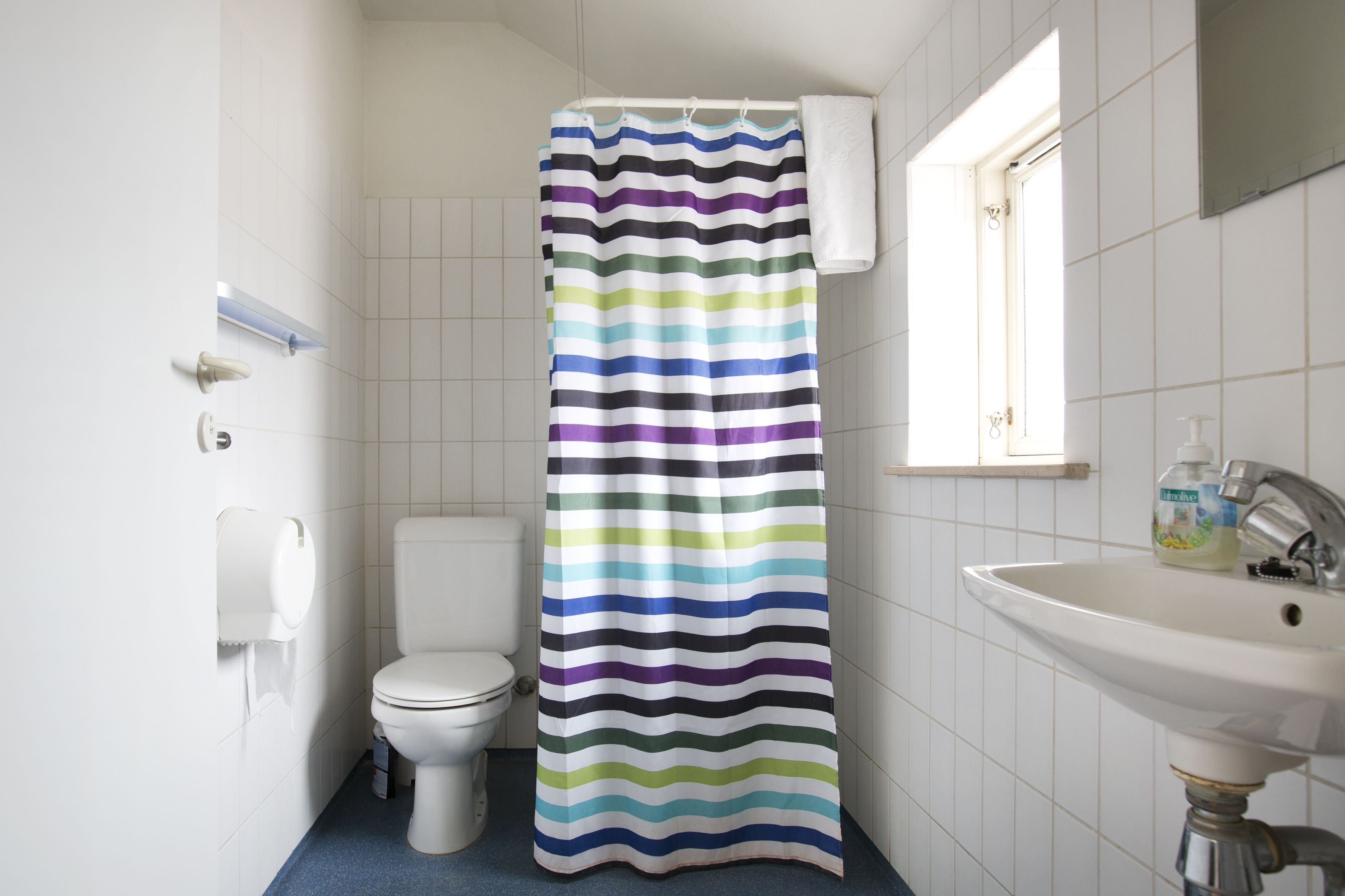 Un baño con cortina de ducha a rayas, inodoro, lavabo y ventana.