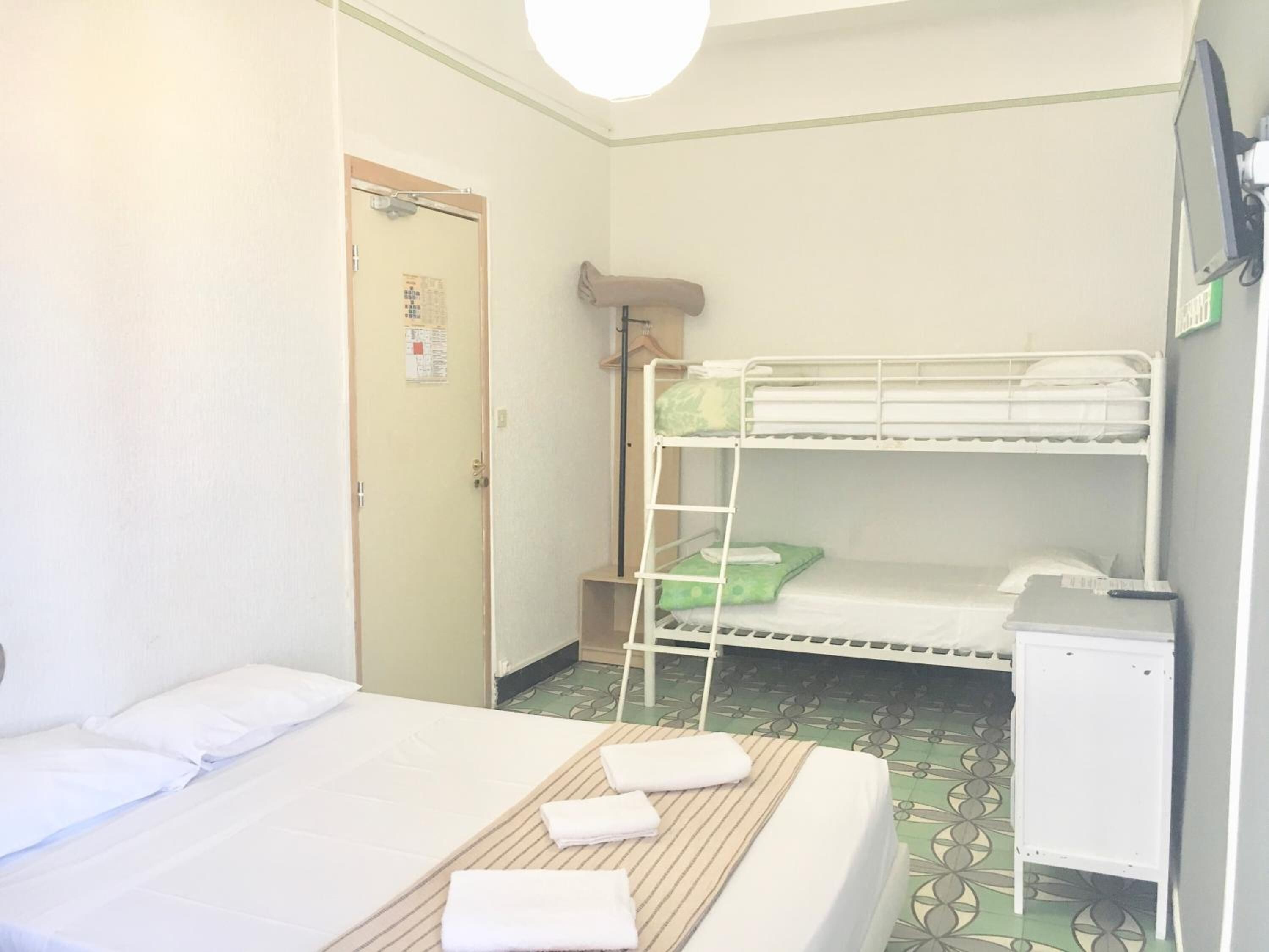 A single-bed room with a bunk bed in the corner, a small desk, and a door with a notice.