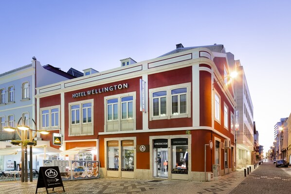 A hotel named HOTEL WELLINGTON with a classic facade, multiple storefronts, and a cobblestone street. - Exe Wellington (Figueira da Foz)