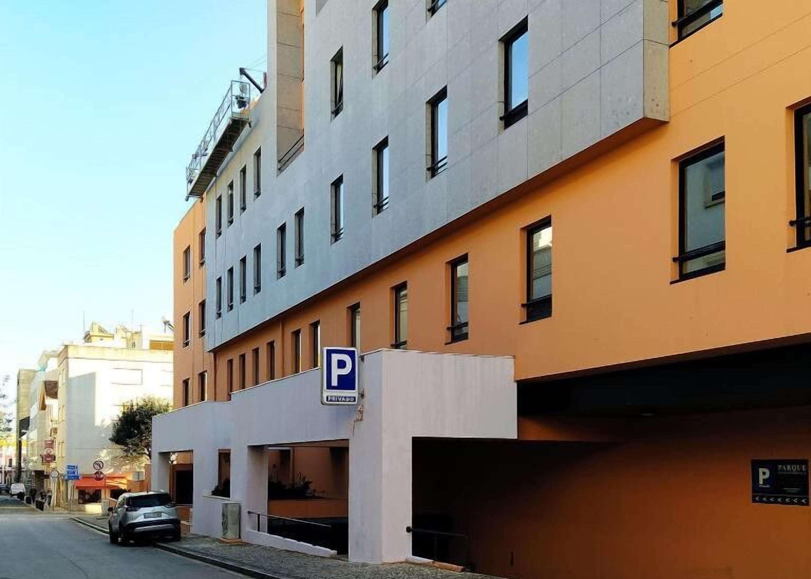 Un edificio de varios pisos con la entrada de un estacionamiento señalada por un cartel con la letra 'P'.