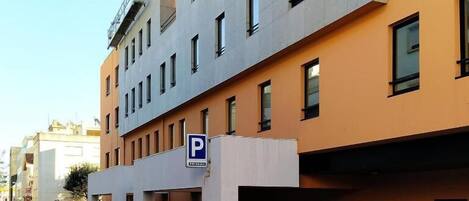 Un edificio de varios pisos con la entrada de un estacionamiento señalada por un cartel con la letra 'P'.