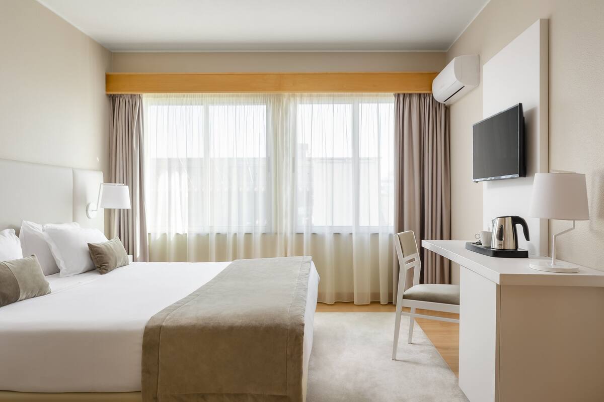 A hotel room with a large bed, a desk with a chair, a television, and a window with curtains.