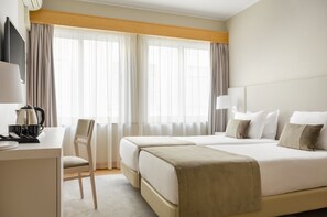 A hotel room with a bed, a desk, a chair, and a TV. - Exe Wellington (Figueira da Foz)