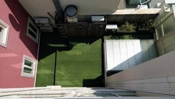 A narrow outdoor space with artificial grass, a white garage door, and a red building wall.