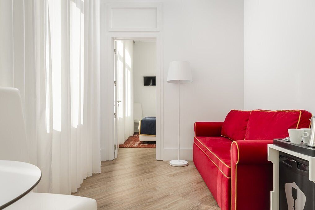 Une chambre d’hôtel moderne avec un canapé rouge, une lampe blanche et un plancher en bois.