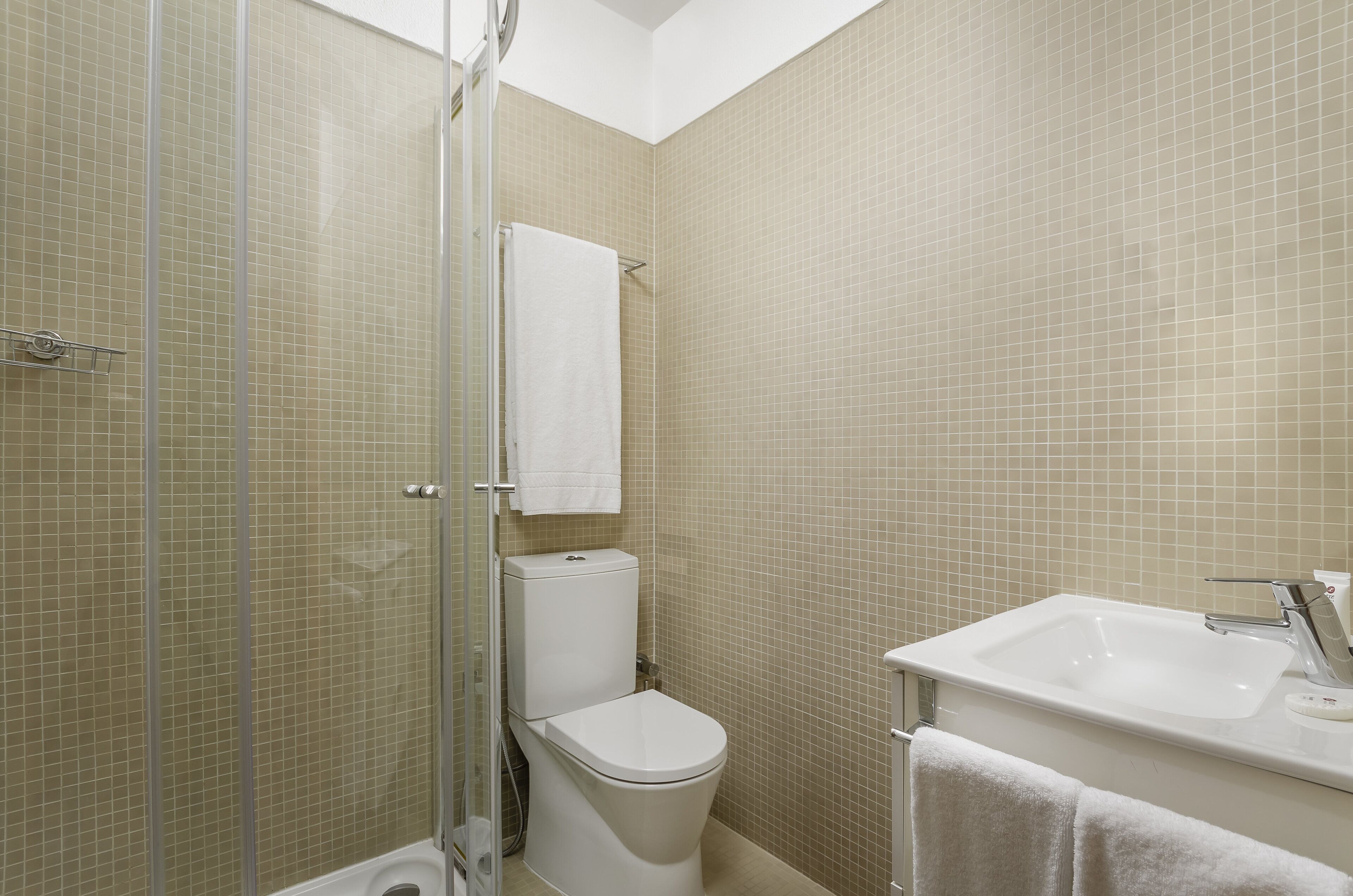 Et badeværelse med brusebad, toilet, håndvask og et brusehjørne med glasvægge.