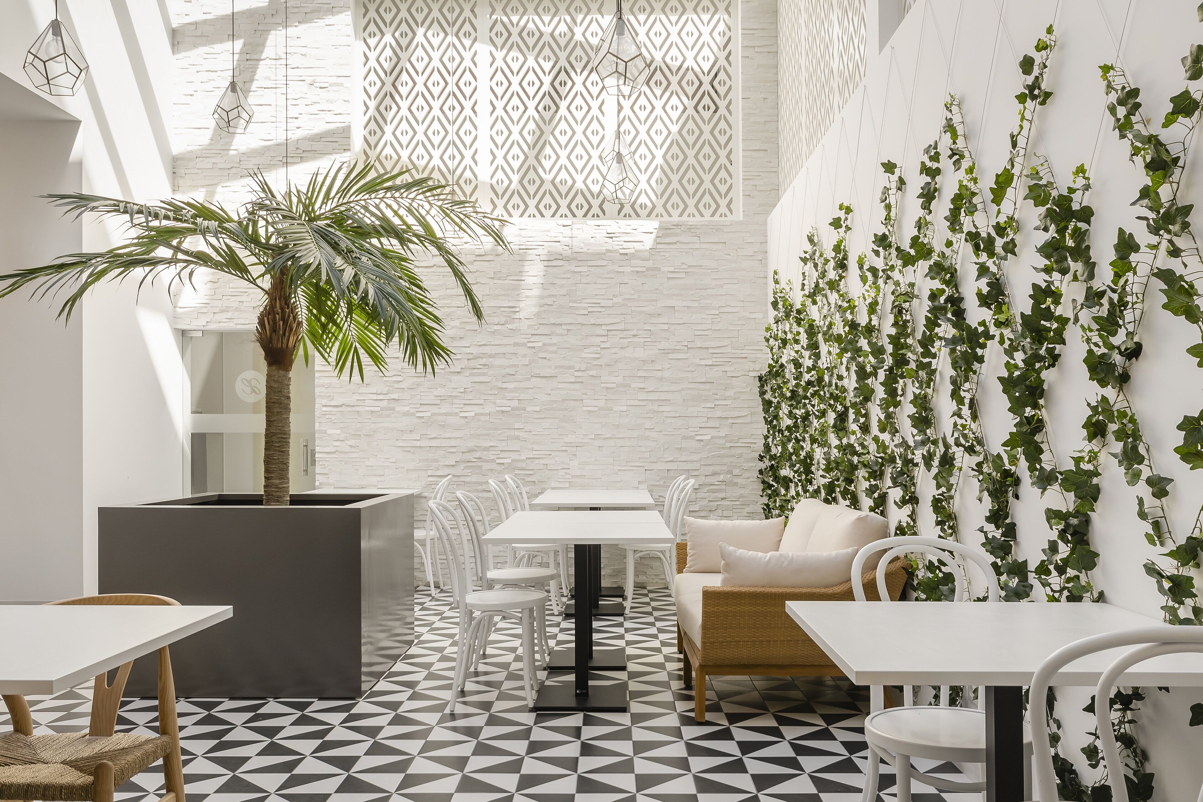 A modern dining area with white furniture, a geometric patterned floor, and a wall covered with green vines.