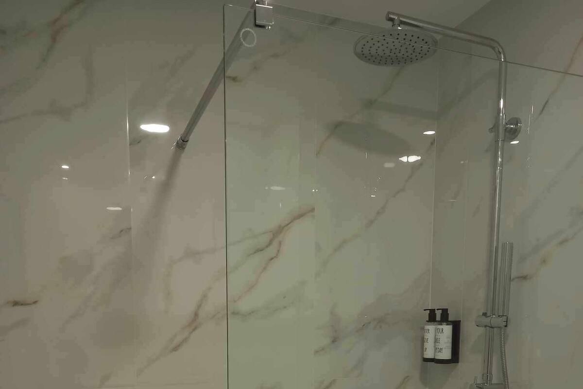 A glass-enclosed shower with a handheld showerhead and a wall-mounted faucet.