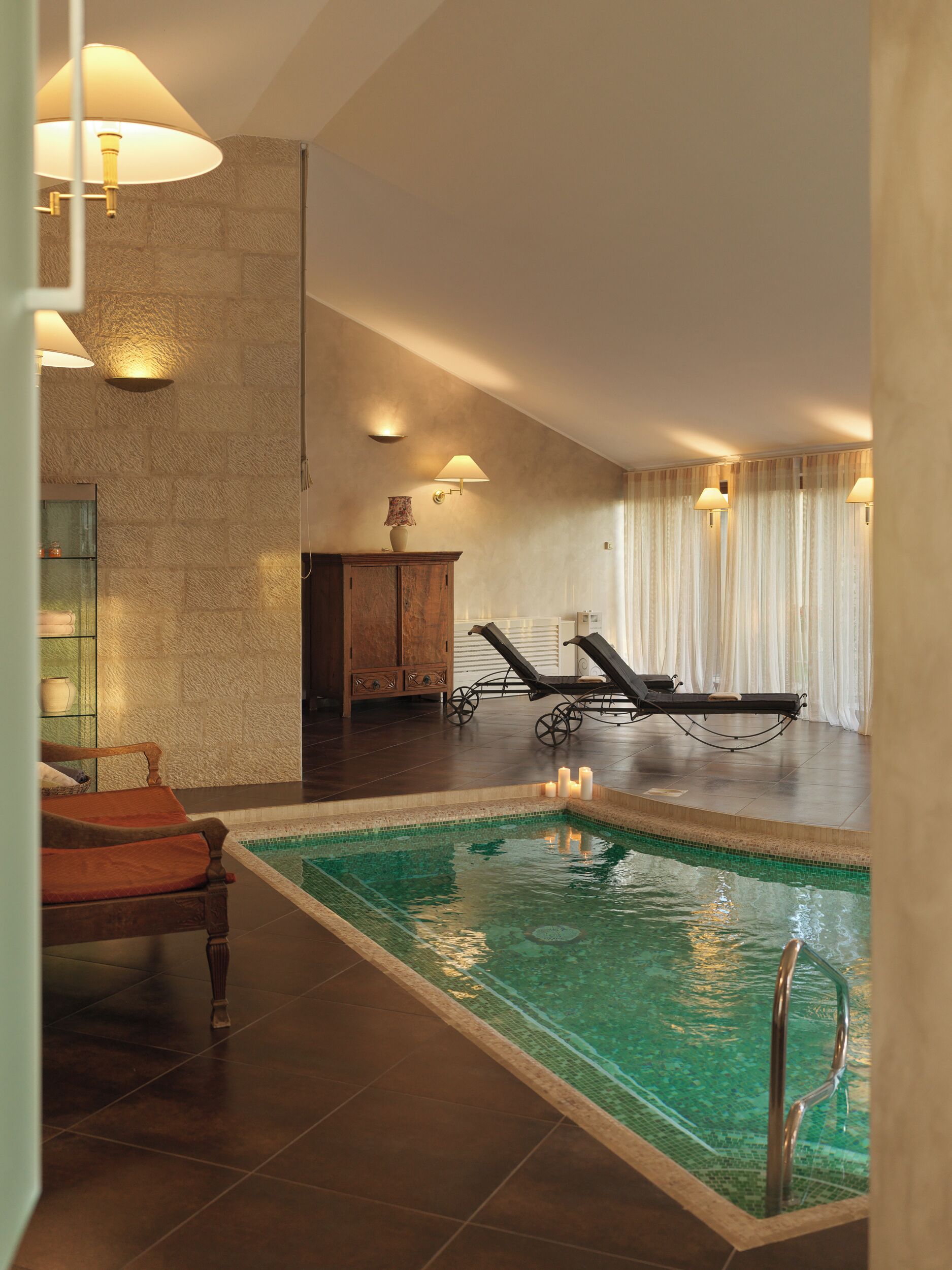 Un espace piscine comprenant des chaises longues, un meuble en bois et des lampes fixées au mur.