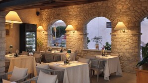 An outdoor dining area with stone arches, wicker furniture, and tables set for dining. - Heritage Hotel San Rocco (Brtonigla)